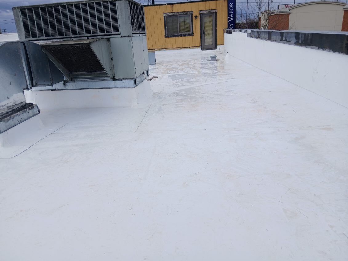 Snow-covered rooftop with a small yellow building and metal equipment under a cloudy sky