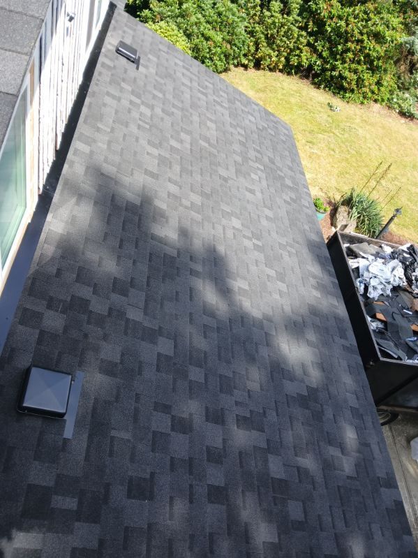 Roof with dark shingles beside a grassy yard and trees, viewed from above.