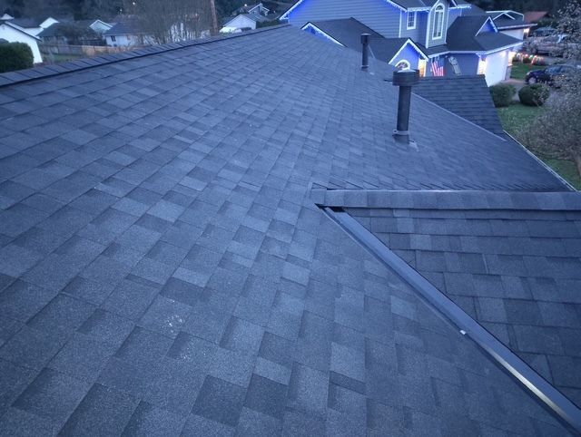 Gray shingled rooftop with a vent pipe, viewed from above at dusk.