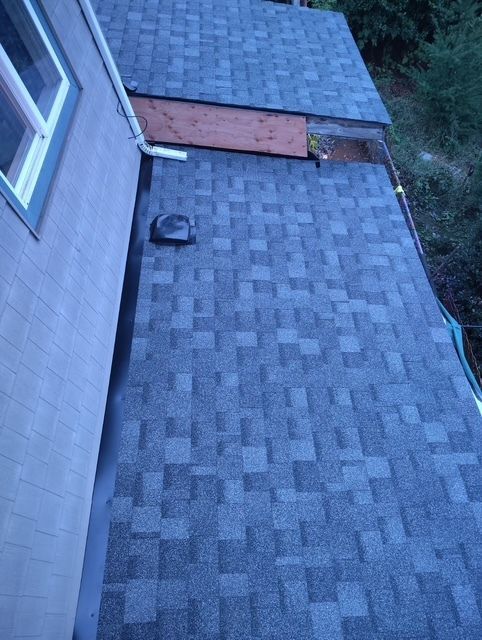 Blue-gray shingled roof beside a house wall, with a small black vent near the edge.