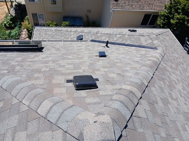 Rooftop shingles with vents and solar conduit near a house garage