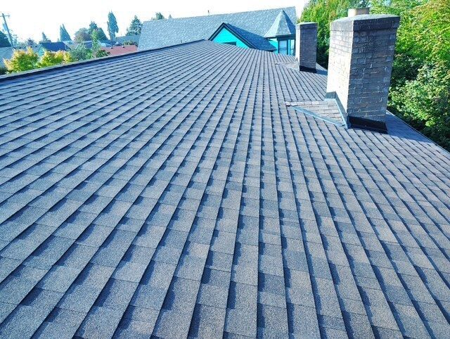 Rooftop with dark shingle roof and two brick chimneys under a clear blue sky