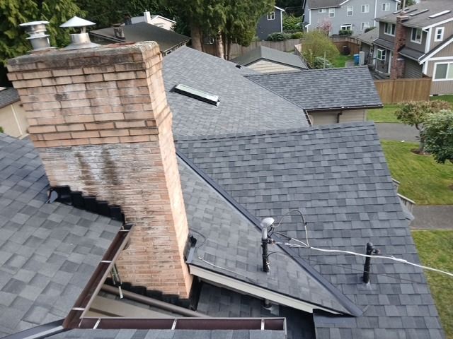 Aerial view of a shingled roof with a brick chimney and power lines over a residential neighborhood