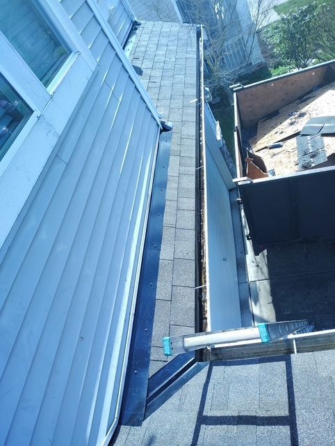 Narrow roof walkway beside blue siding, with gutter and neighboring rooftop visible.