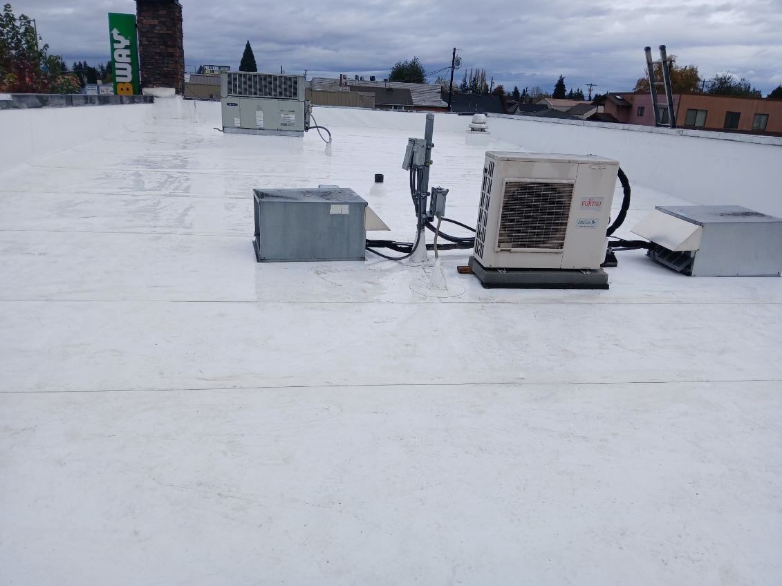 Rooftop with HVAC units and vents on a snowy, flat roof under a cloudy sky.