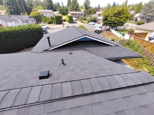 Roof with dark shingles and vents in a suburban neighborhood, viewed from above
