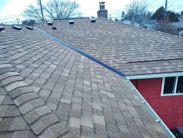 Roof shingles on a house with a blue rope or cable stretched across them, beside a red siding wall.