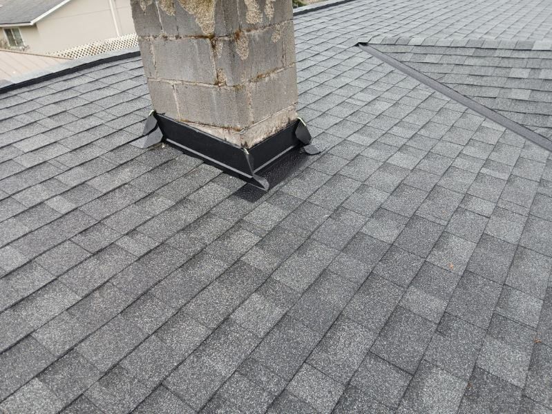 Damaged chimney flashing on a gray shingle roof, with cracked chimney masonry.