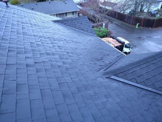 Rooftop view of dark gray shingles overlooking a residential street and driveway