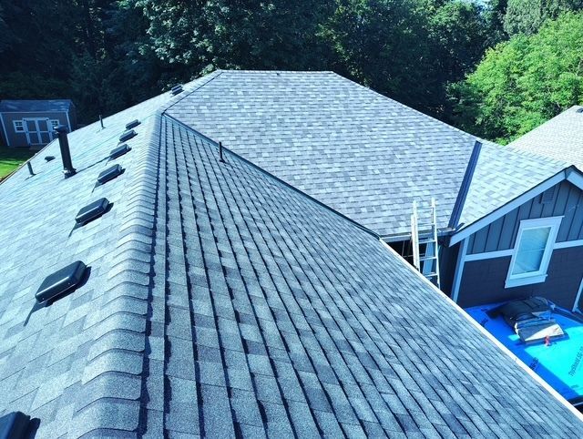 View from roof ridge over gray shingles and skylight to a house and blue pool below