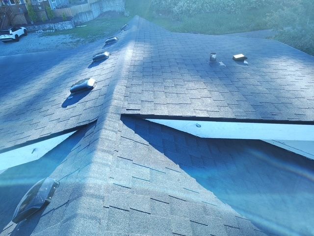 Blue asphalt shingle roof with vents and a valley seam, viewed from above