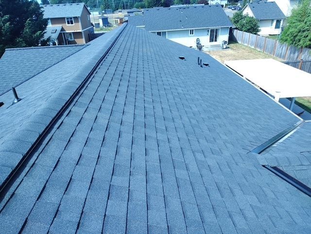 Roof covered with dark gray shingles, viewed from above in a suburban neighborhood.