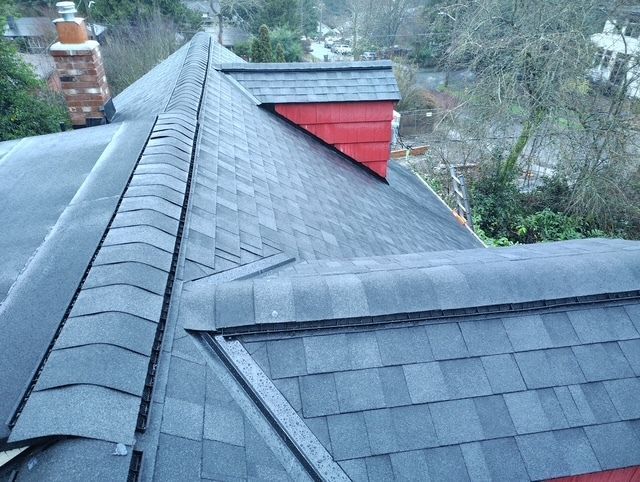 Roof with dark gray shingles and a red dormer on a wooded hillside