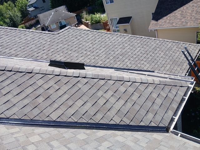 Roof with gray shingles and a long white skylight vent on a sloped house roof