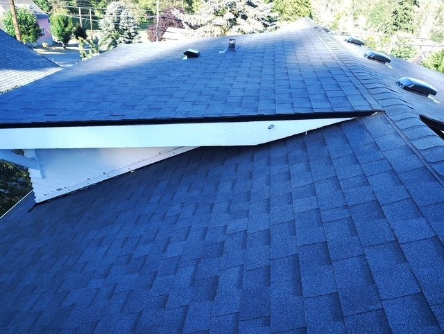 A rooftop skylight or panel lifted open on a blue shingled roof, exposing the interior edge.