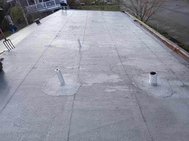 Flat rooftop with several vent pipes and patched roofing sections, viewed from above.