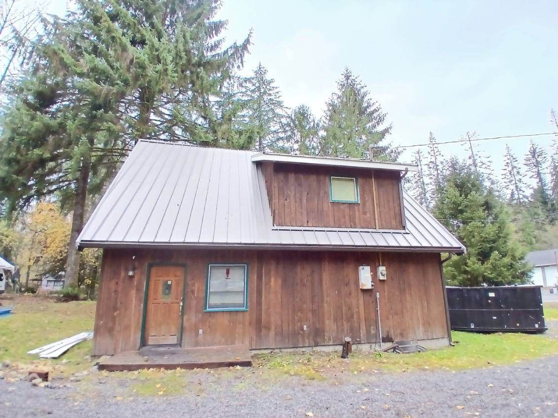 Small weathered wooden cabin with a metal roof, set among trees on a gravel lot.