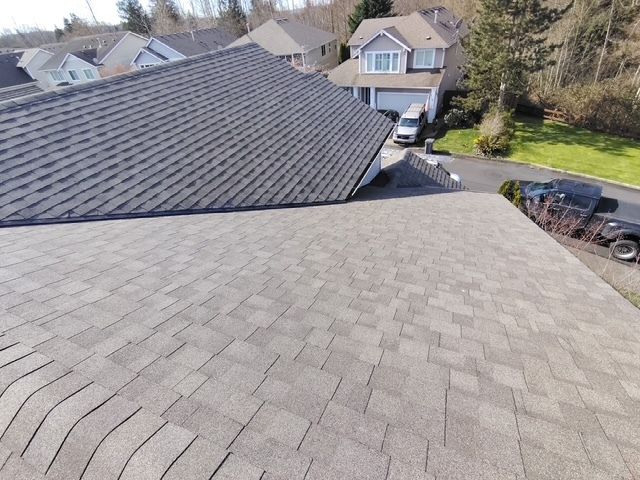 Residential neighborhood seen from a rooftop with gray asphalt shingles and parked cars below