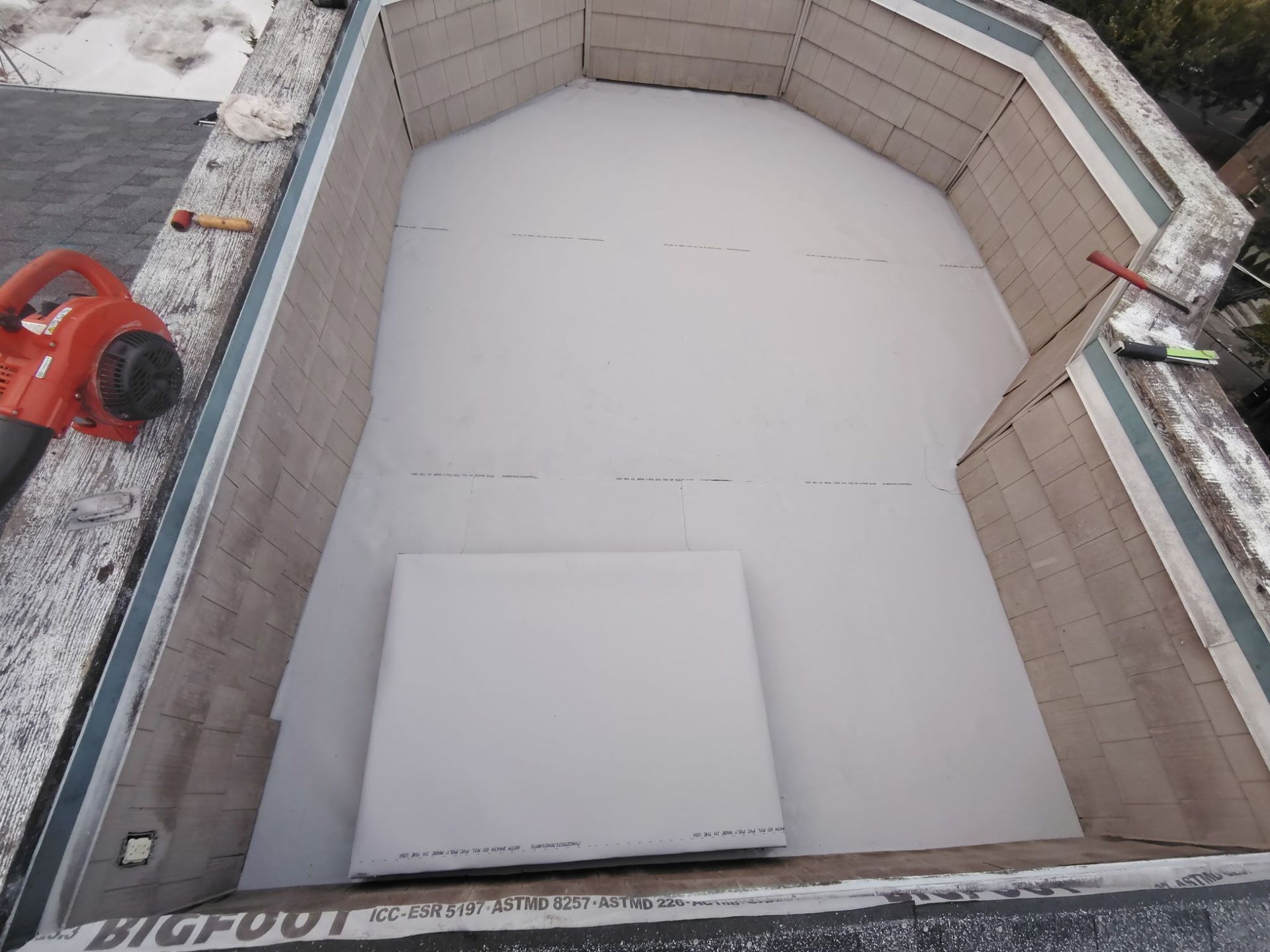 Empty rooftop pool or basin lined with white material, viewed from above, with a red tool on the left edge