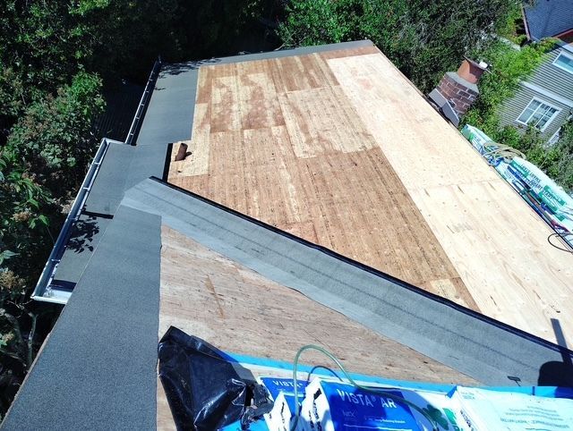 Roof under construction with plywood sheathing and dark shingles along one edge