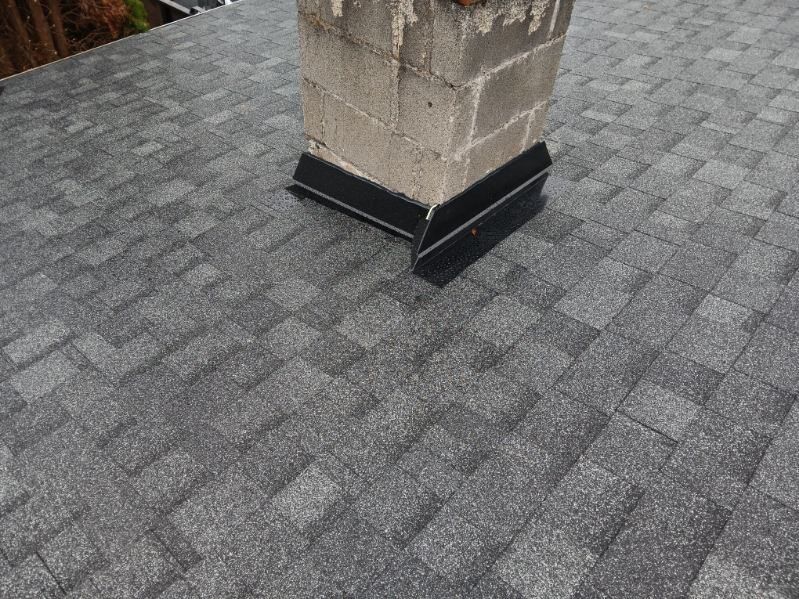 Gray shingled roof with a stone chimney wrapped in black flashing.