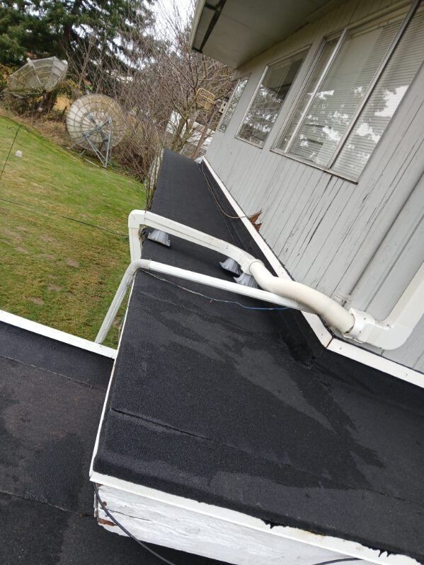 Rooftop with black flat roofing, white trim, and a white vent pipe beside gray siding and windows.