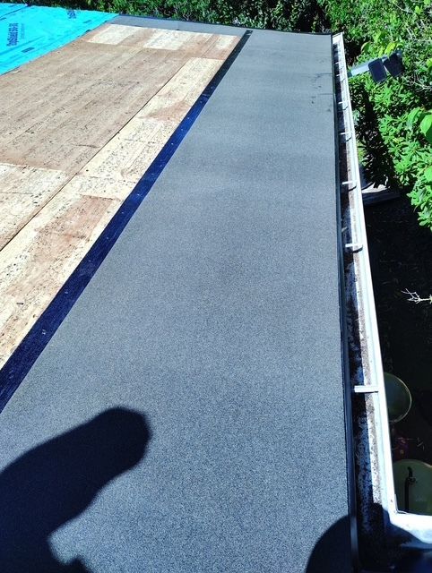 Rooftop walkway with gray waterproof membrane beside a wooden deck and greenery