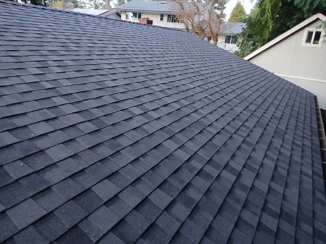 Dark gray shingled roof on a house, viewed from above with neighboring homes in the background
