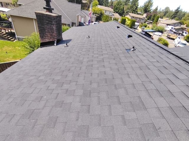 View from a rooftop with gray asphalt shingles, a chimney, and nearby homes in a suburban neighborhood