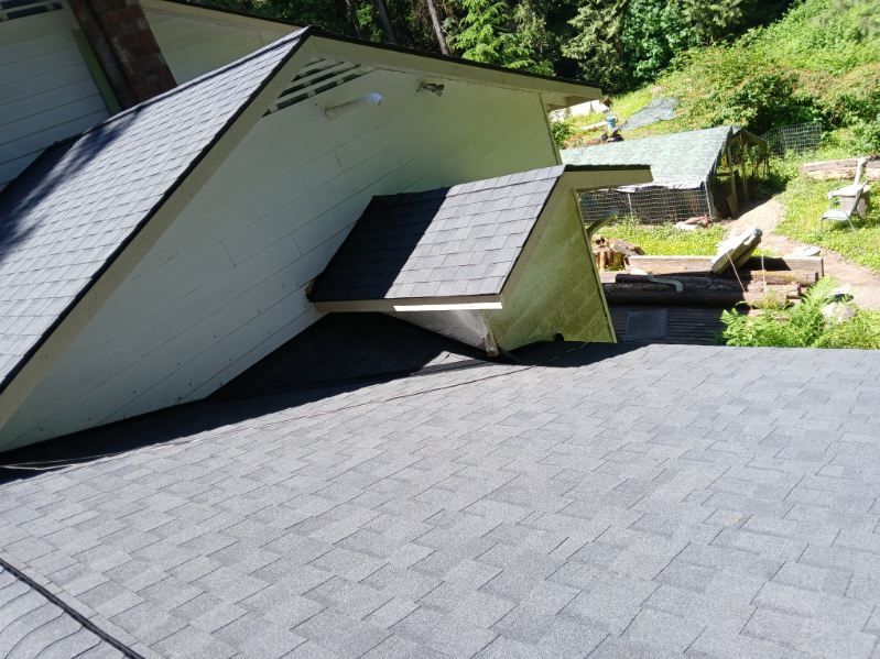 Roof with gray shingles and dormer windows on a house beside a green hillside