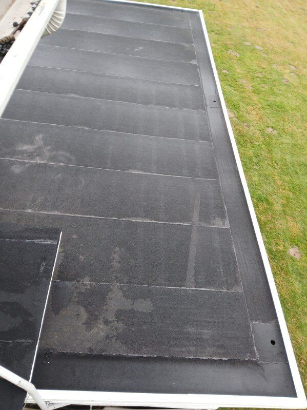 Black flat roof with white edging next to a grassy area, viewed from above