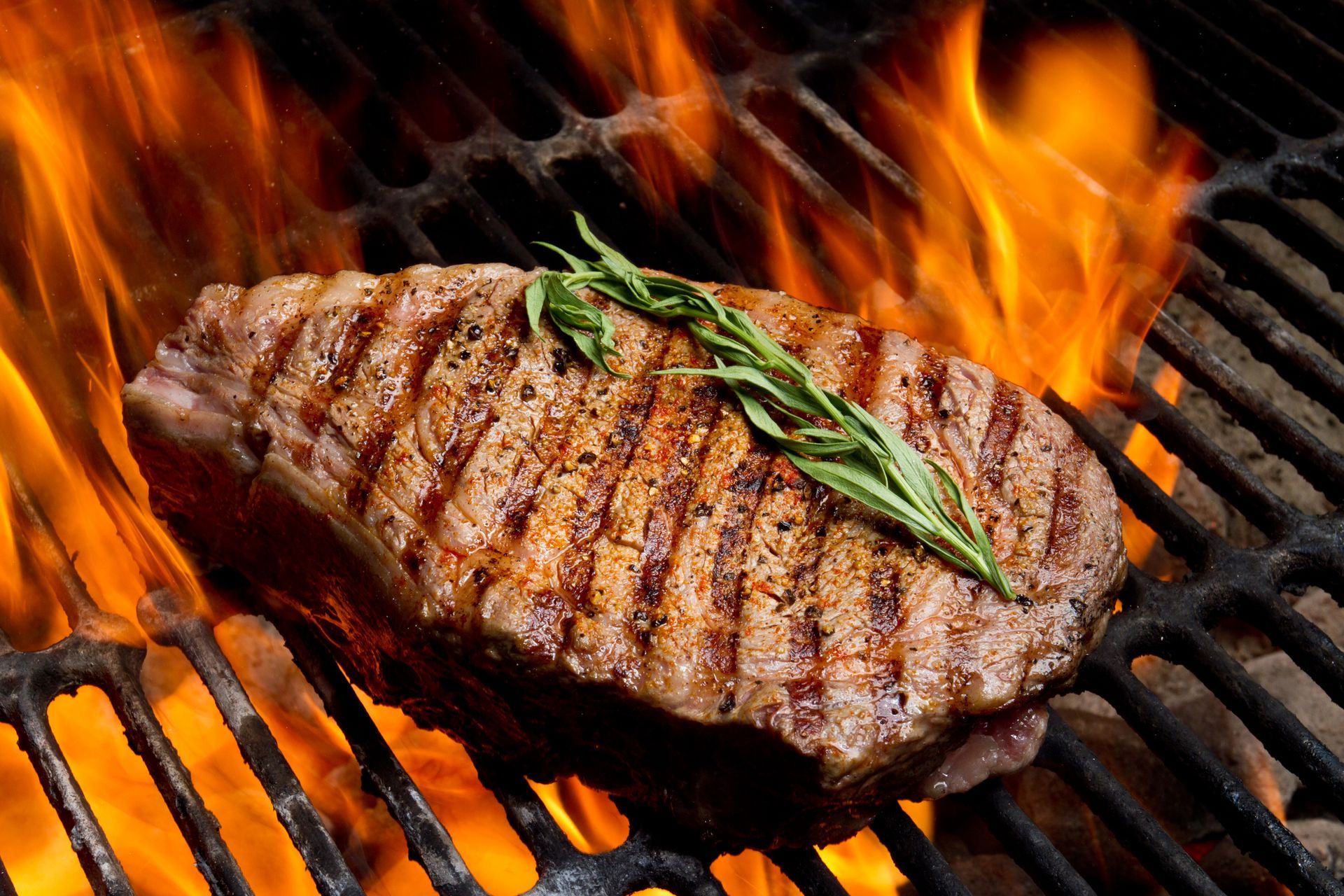 Bistecca alla griglia con i segni della griglia, guarnita con rosmarino, su una griglia ardente.