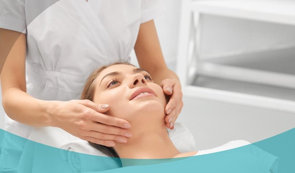 In un ambiente luminoso e clinico, una persona in abbigliamento professionale esegue un delicato massaggio al viso su un cliente rilassato.