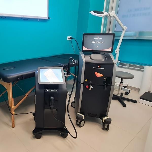 Due apparecchi laser per uso medico estetico in una stanza ben illuminata con pareti color verde acqua e un lettino per le visite.