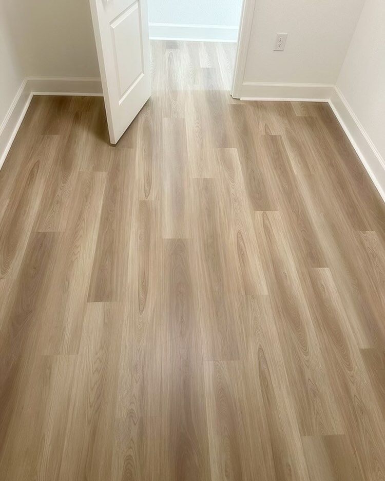 Empty room with light wood flooring, white walls, and an open door leading to a bright hallway