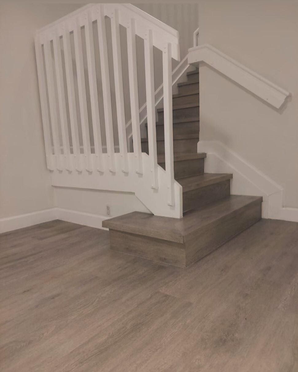 White staircase with gray steps and railing in a beige room with wood-look flooring