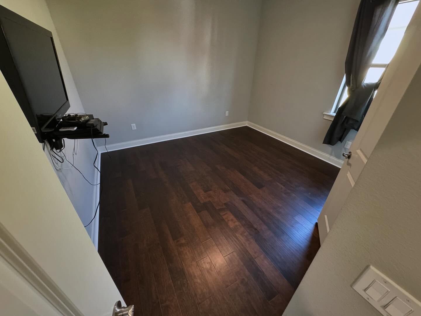 Empty room with dark wood floor, gray walls, and a window with curtains.