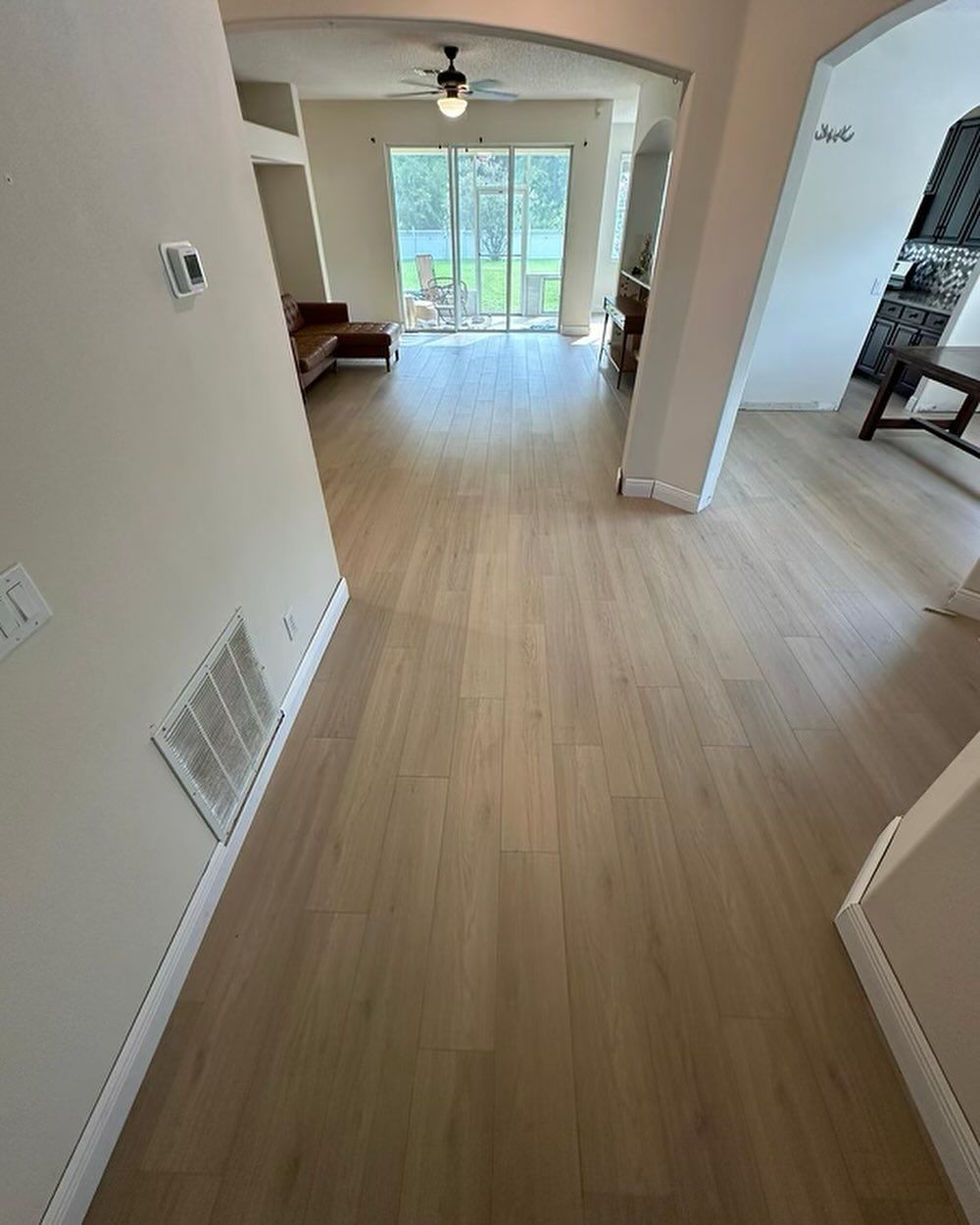 Empty hallway with light wood floors, white walls, and sliding glass doors at the far end.