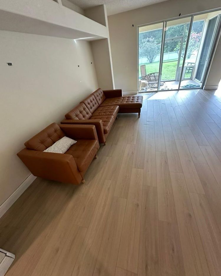 Bright living room with brown sectional sofa, light wood floor, and large glass doors to a patio.