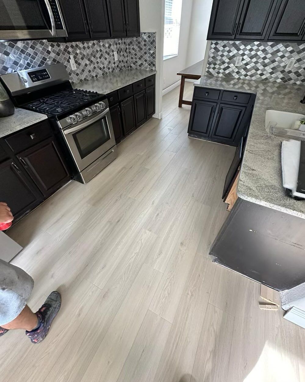 Modern kitchen with dark cabinets, granite counters, stainless oven, and light wood floor.