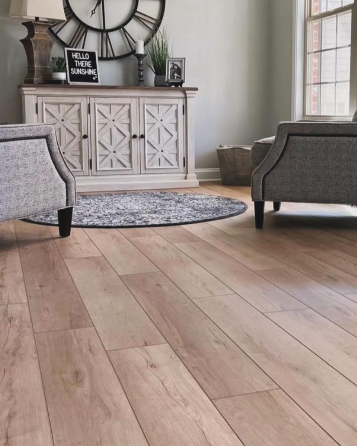 Bright living room with wide plank wood floor, gray chairs, white cabinet, and round rug