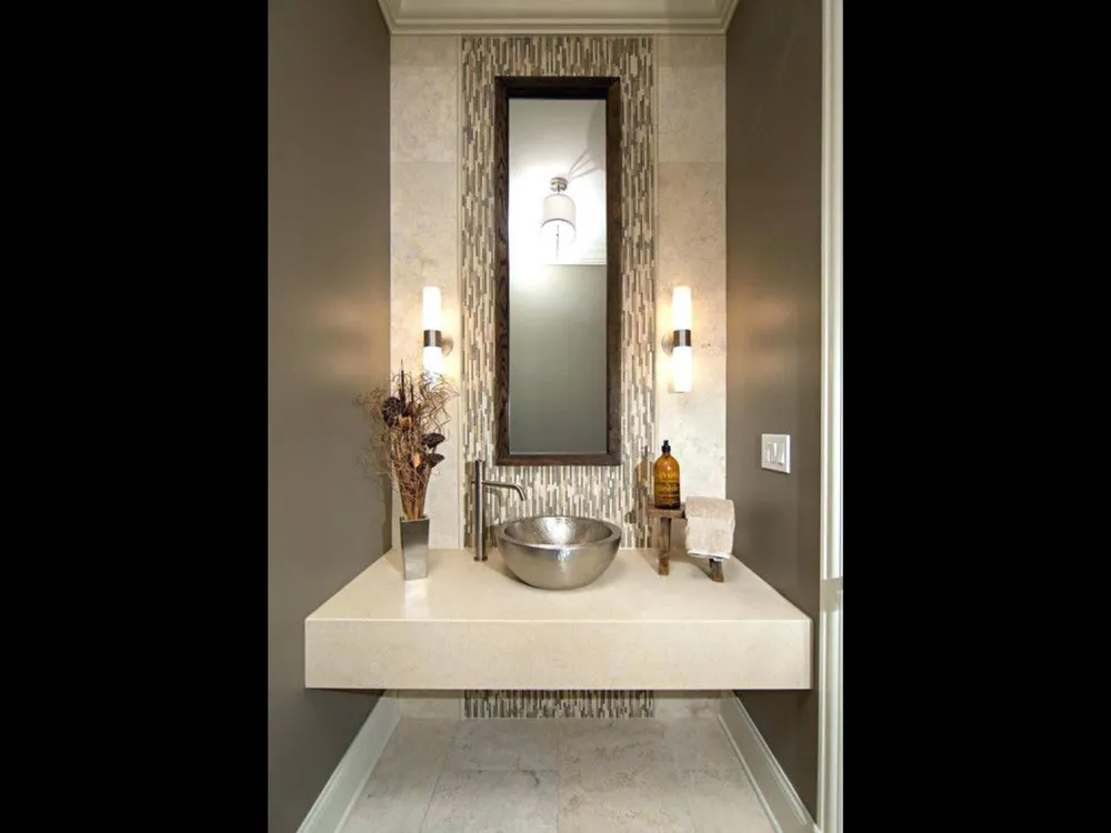 Small powder room vanity with rectangular mirror, wall sconces, and decorative vases on a white countertop.