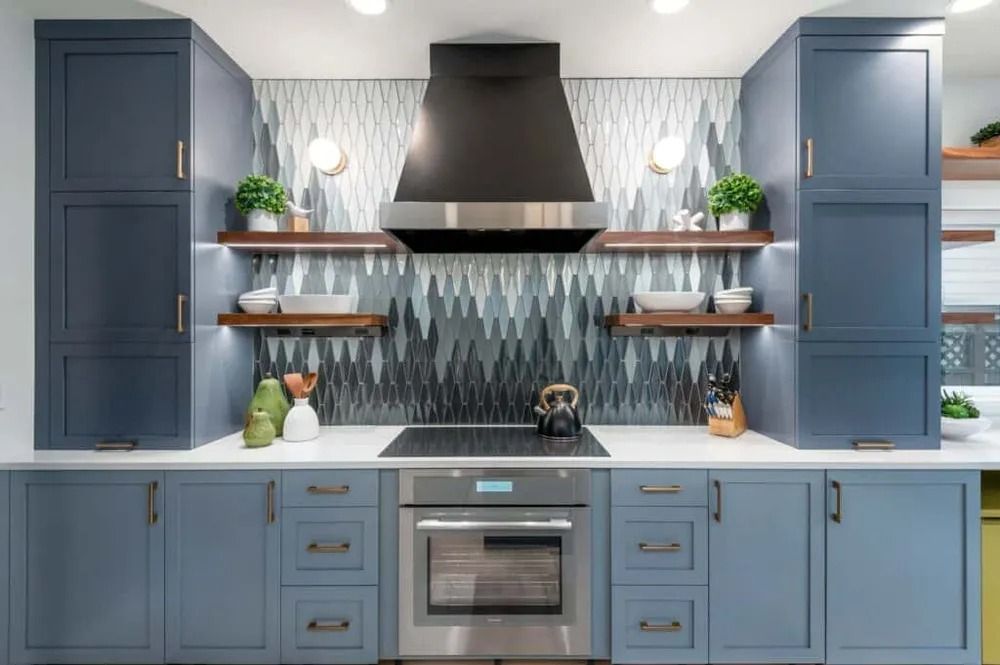 Modern blue kitchen with black range hood, white countertop, open shelves, and stainless oven