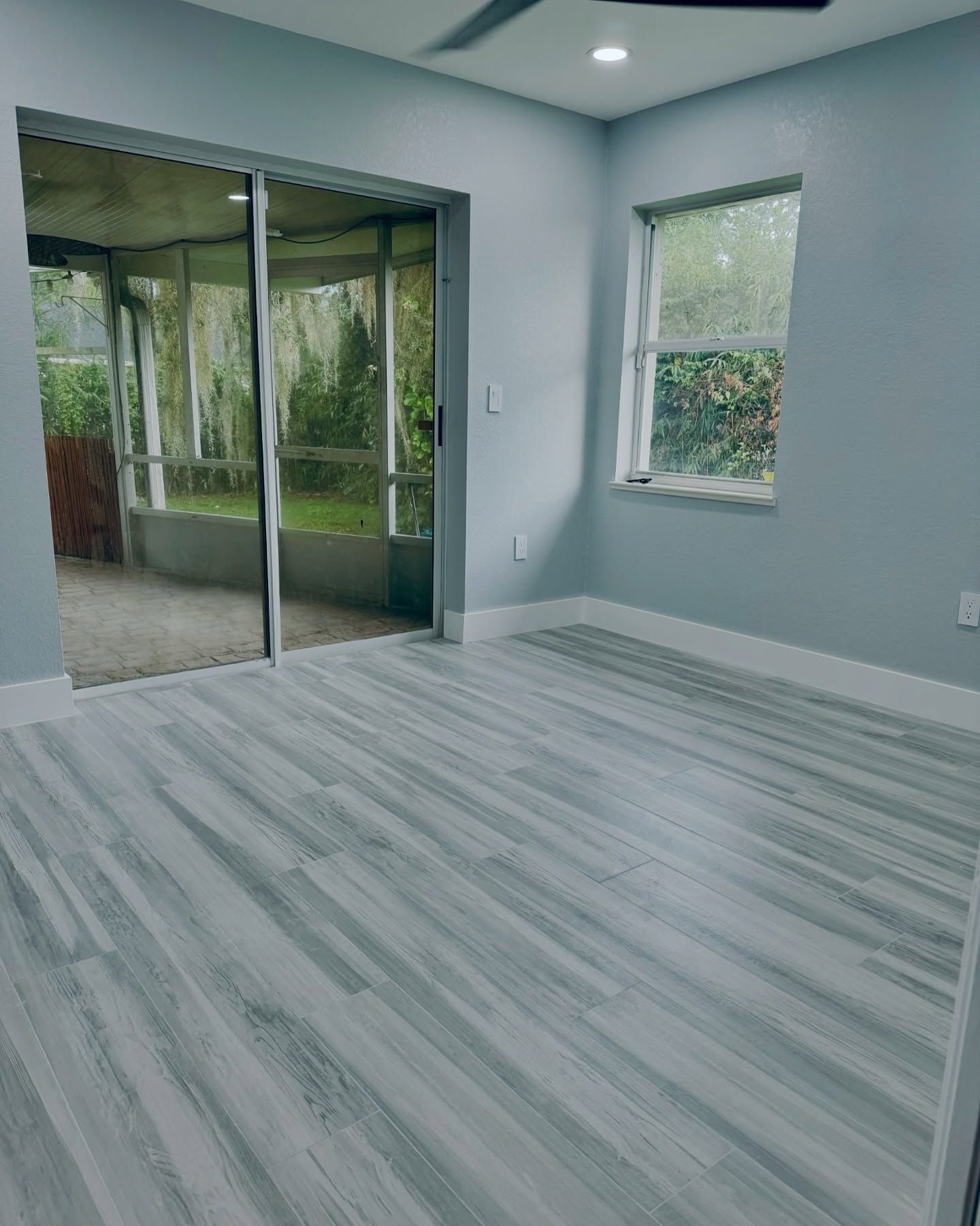 Empty modern room with light gray walls, striped flooring, window, and sliding glass doors to a patio.
