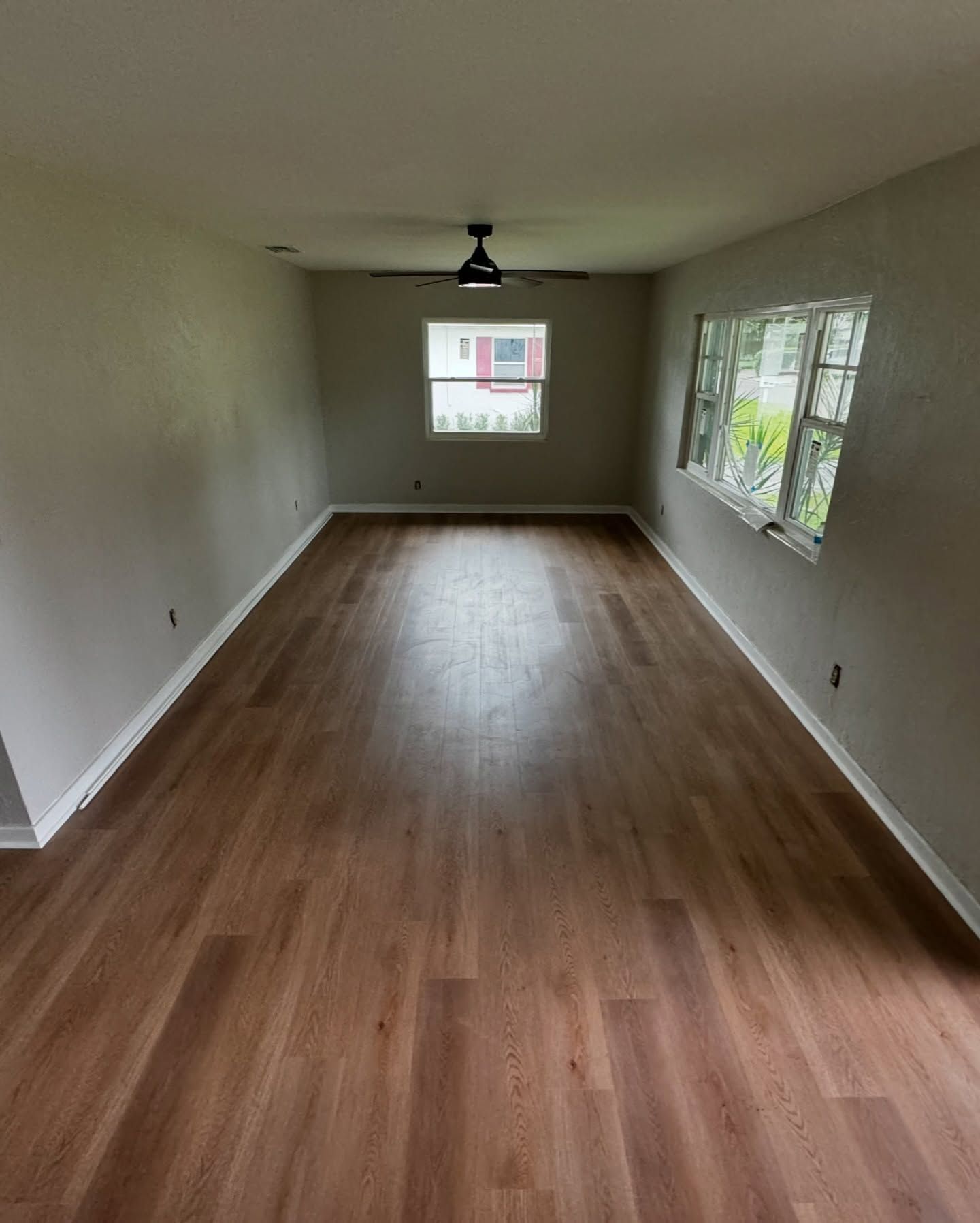 Empty living room with wood floors, beige walls, and windows letting in daylight.