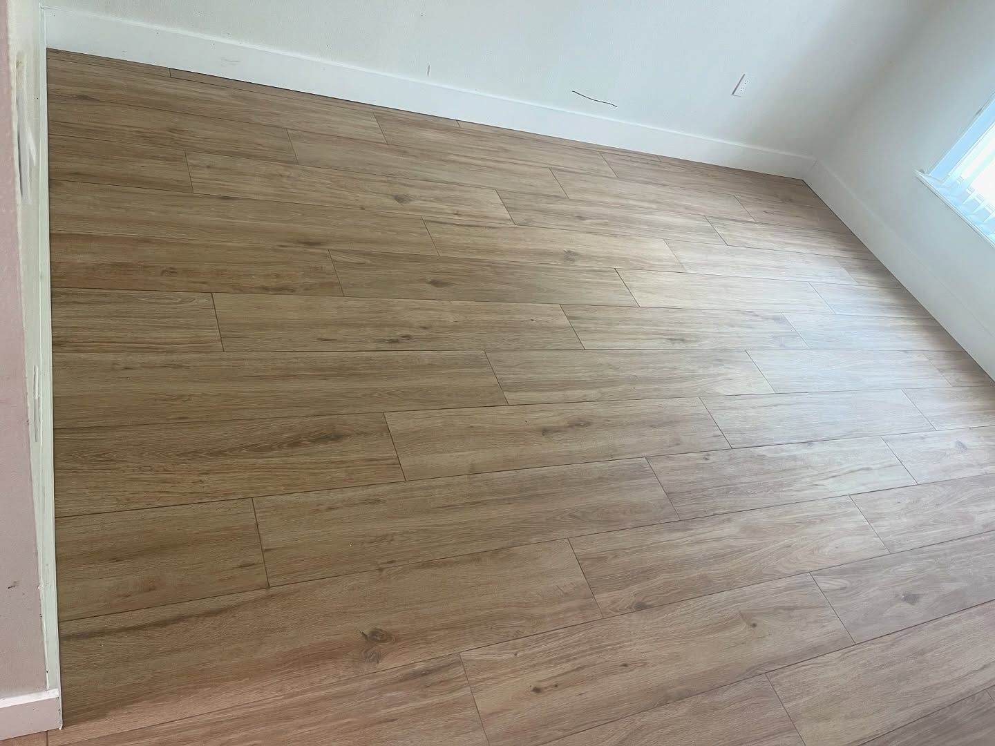 Empty room with wood-look flooring and white walls, lit by natural light.
