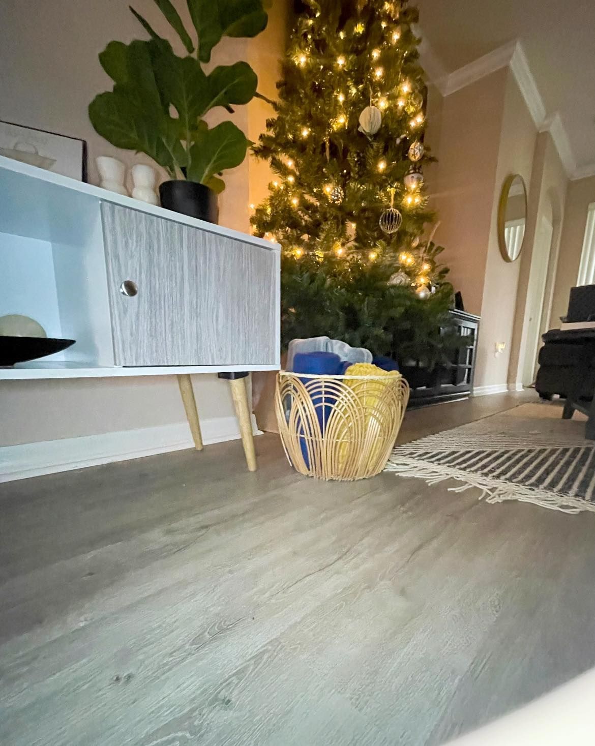 Living room with lit Christmas tree, woven basket, sideboard, and rug on wood flooring