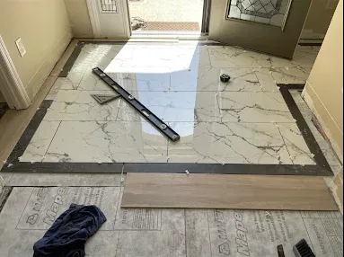 Entryway floor with partially installed marble tile, loose trim piece, and tools nearby.