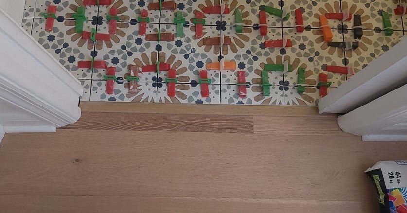 Wooden floor beside a colorful patterned rug with white doorframes on both sides.