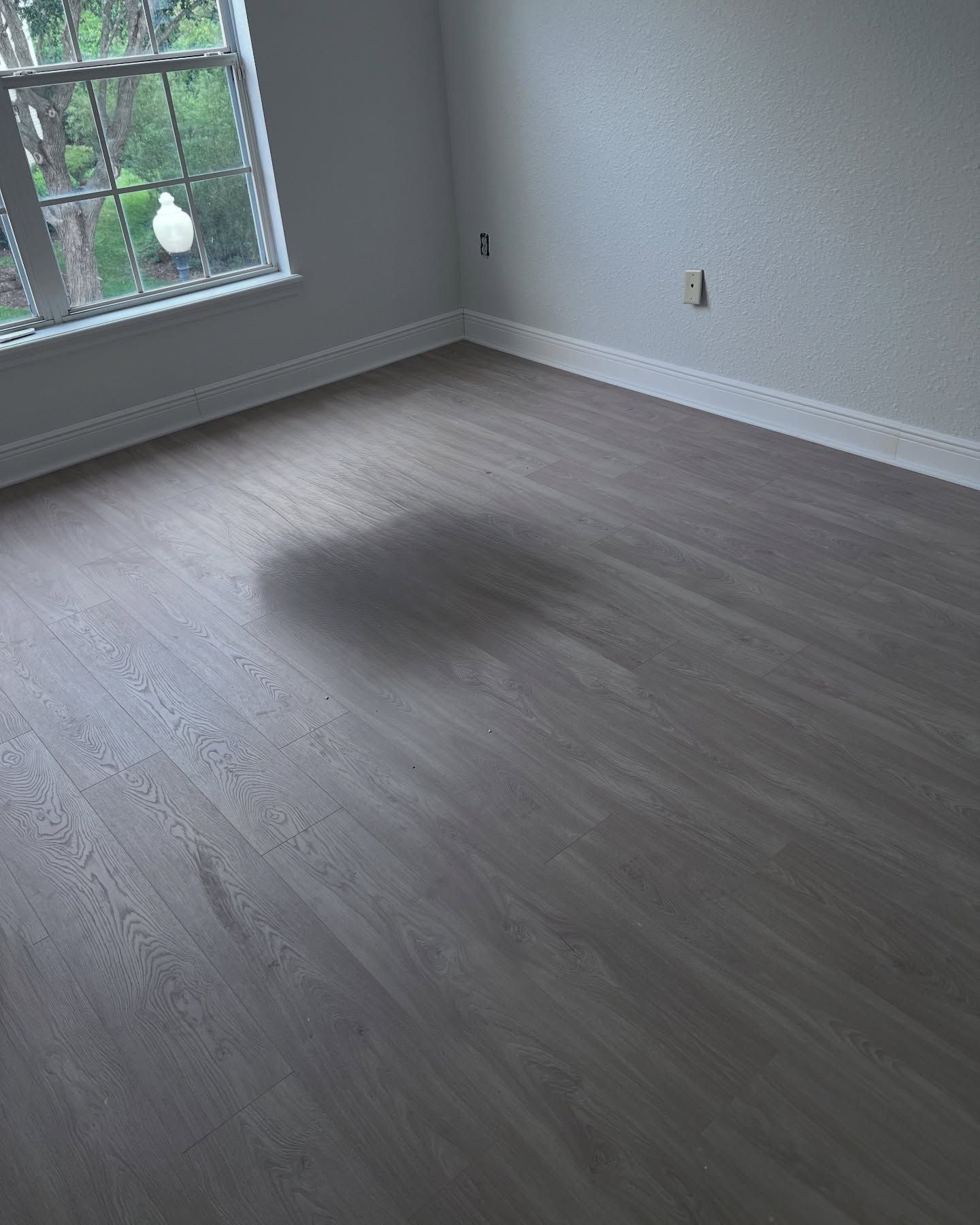 Empty room with gray wood flooring, white walls, and a window letting in daylight.